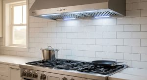Stainless steel wall-mounted kitchen exhaust fan with LED lighting installed above gas range cooktop for effective smoke and grease removal